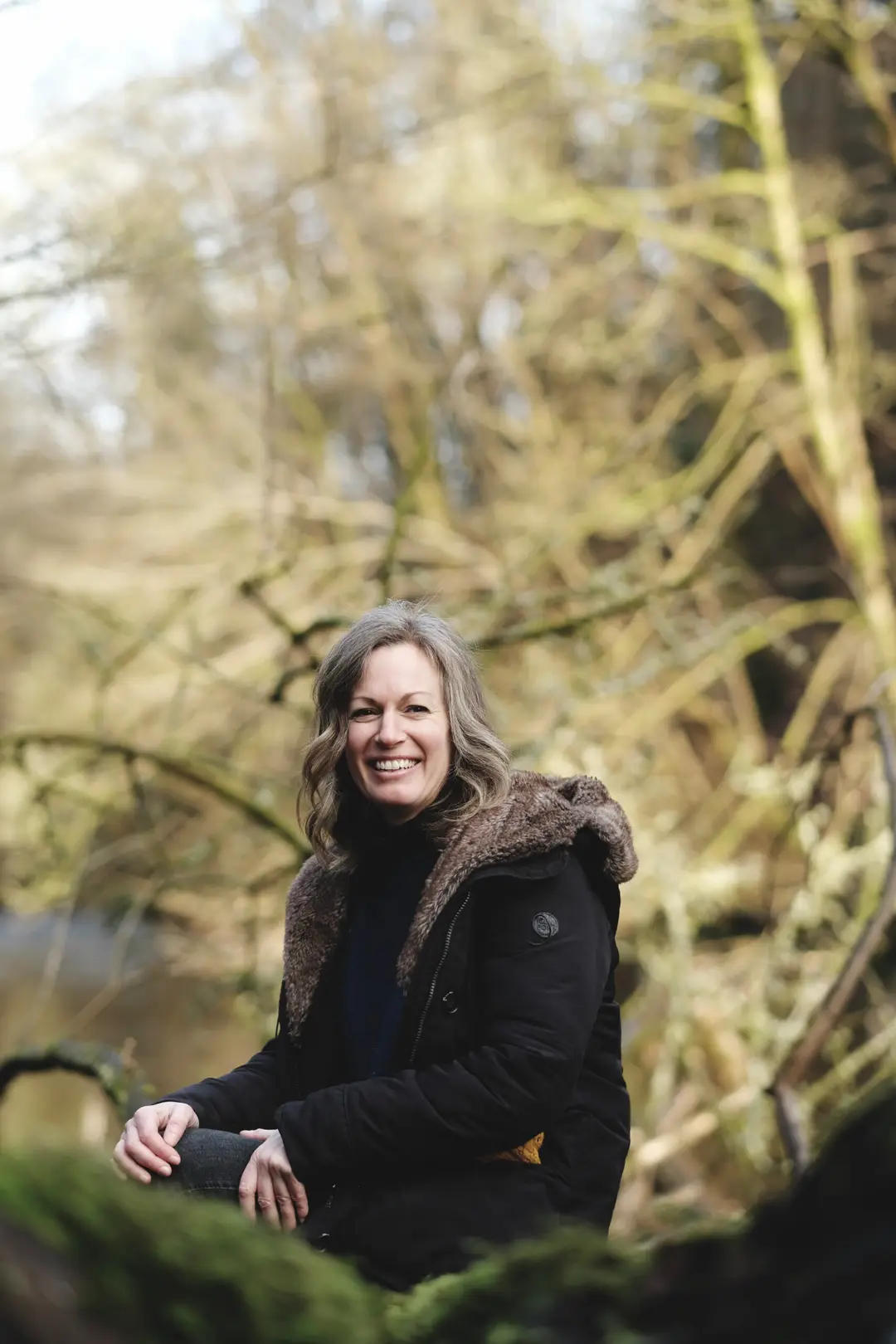 Nicki sitting among the trees and moss of a Renfrewshire woodland, smiling